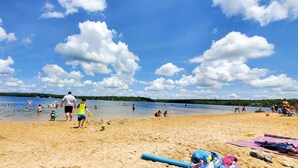 A beach scene with people swimming and playing in the water, a sandy shore, and a clear blue sky with clouds.