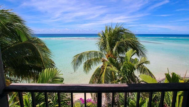 Une vue sur une plage tropicale, avec une eau turquoise cristalline, des palmiers et une balustrade en bois.