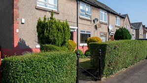 A row of terraced houses with a gated entrance, a small garden, and a clear blue sky.