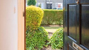 A view through a door into a garden with neatly trimmed hedges and a residential building in the background.