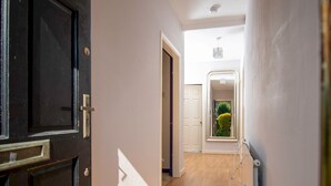 A hallway with a black door, white walls, and a wooden floor.