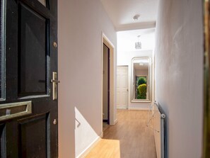Un pasillo con una puerta negra, paredes blancas y suelo de madera.