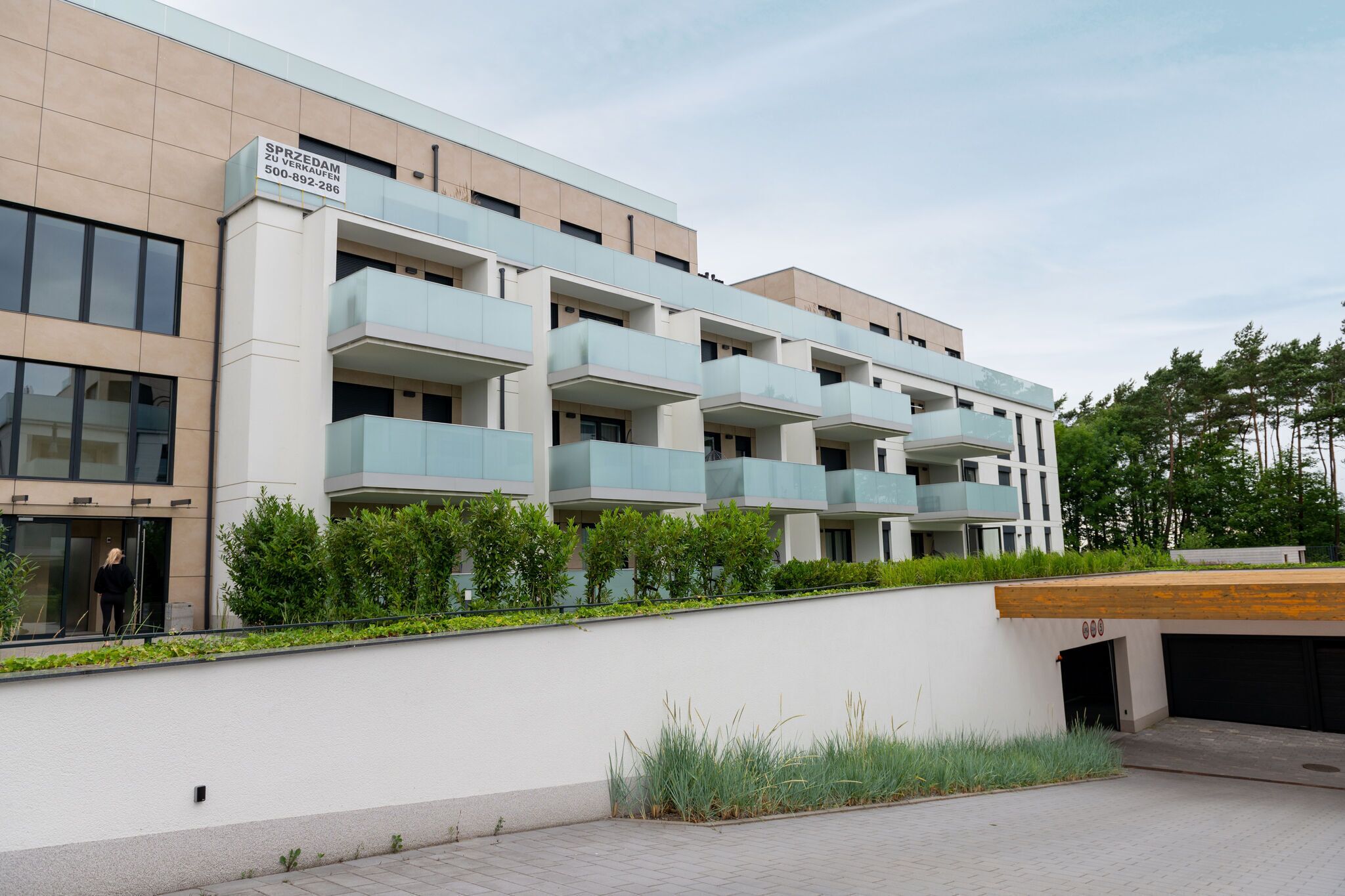 A modern multi-story building with a sign indicating "SPRZEDAM ZU VERKAUEN" and a contact number.
