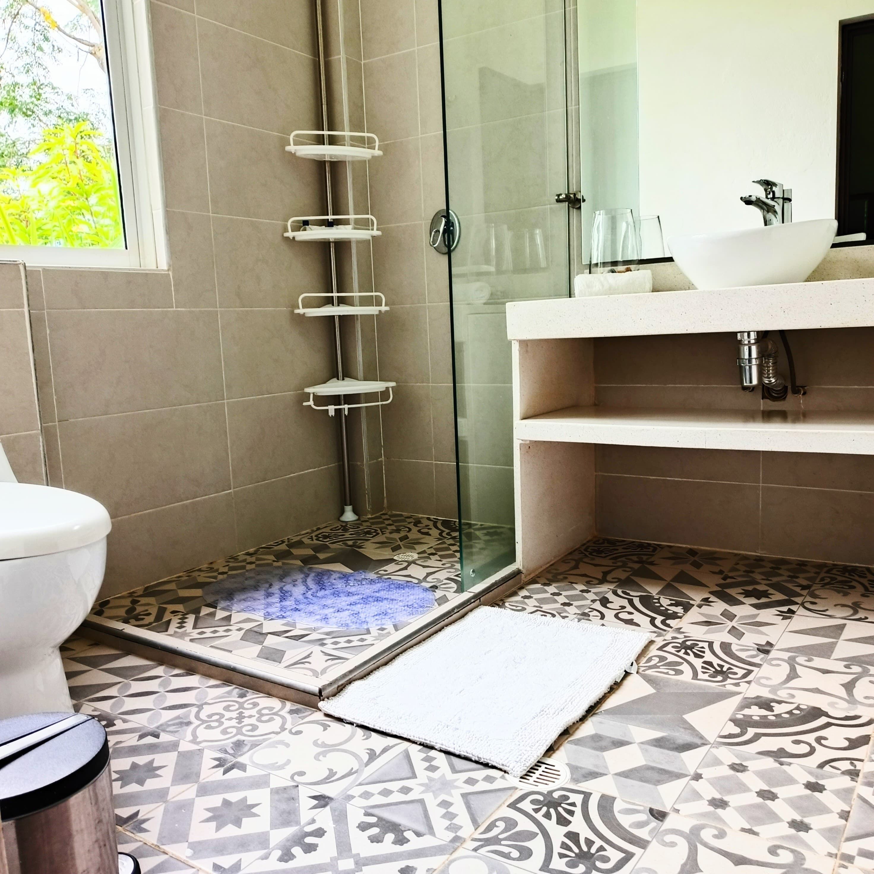 Une salle de bain avec une douche à parois de verre, un lavabo blanc et des carreaux de sol à motifs.