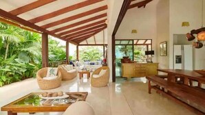 Amplia sala de estar con techo alto, vigas de madera y vistas a exuberante vegetación.