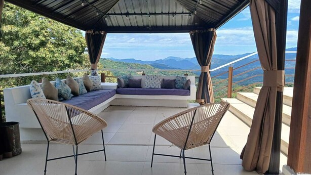 Un espacio de estar techado al aire libre con un sofá y dos sillones, con vistas a un paisaje montañoso.