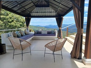 Un espacio de estar techado al aire libre con un sofá y dos sillones, con vistas a un paisaje montañoso.