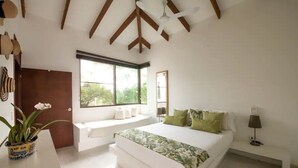 Un dormitorio con una cama grande, un rincón con ventanales y un ventilador de techo.