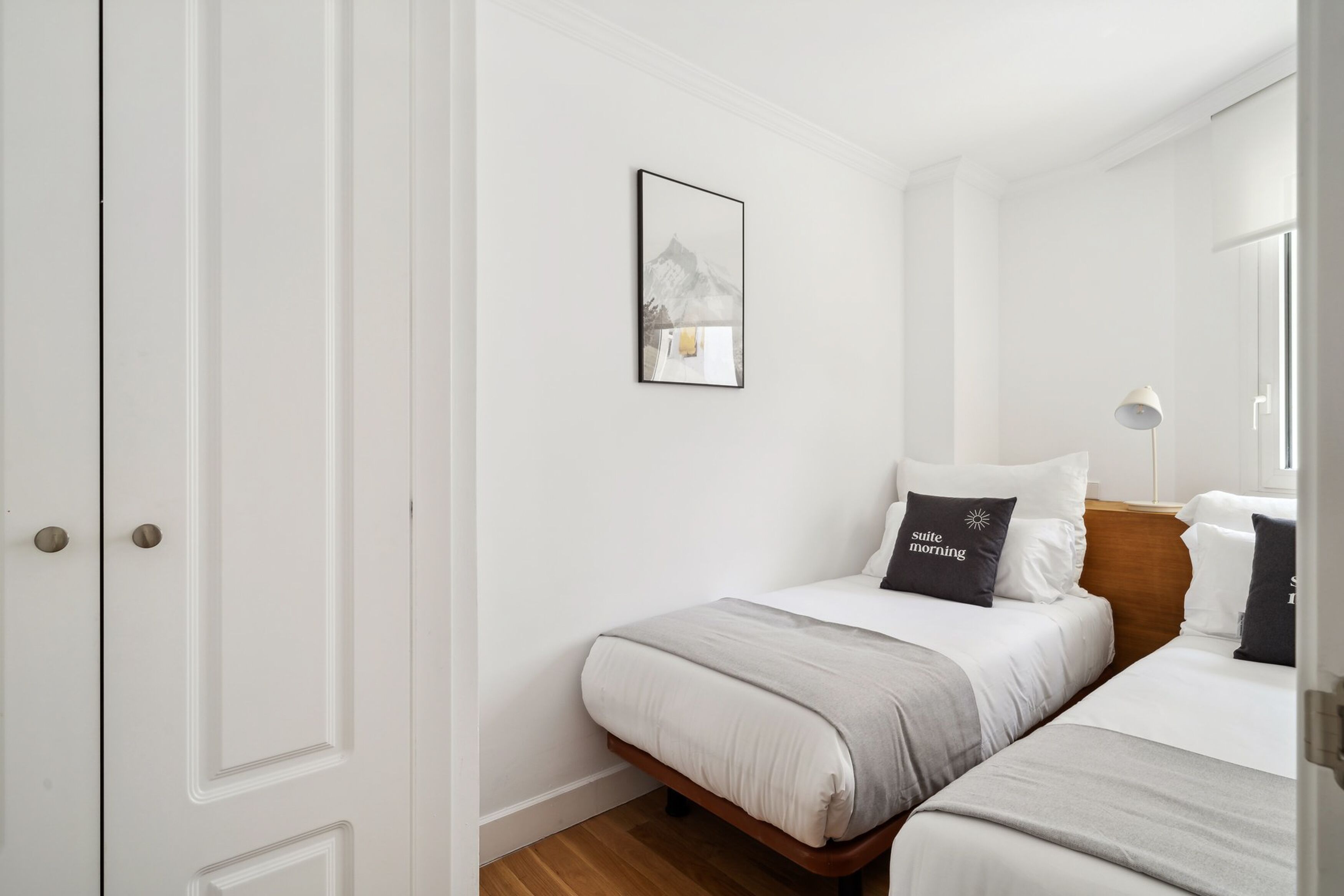 Quarto de hotel com cama, mesa de cabeceira, abajur e um quadro na parede.