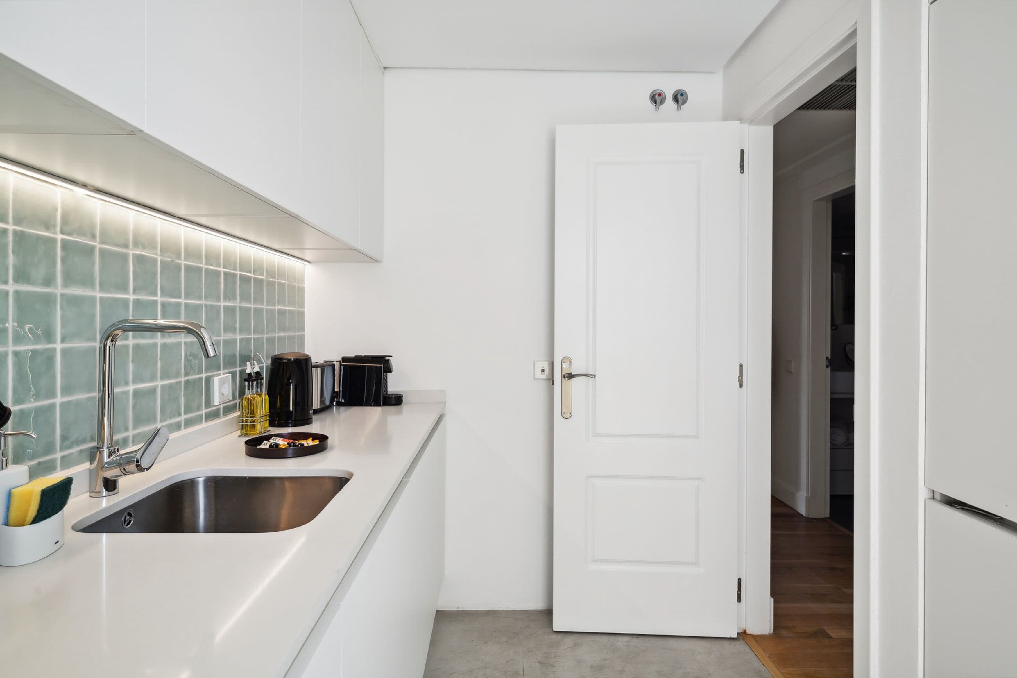 A modern kitchen with white cabinetry, a stainless steel sink, and a tiled backsplash.