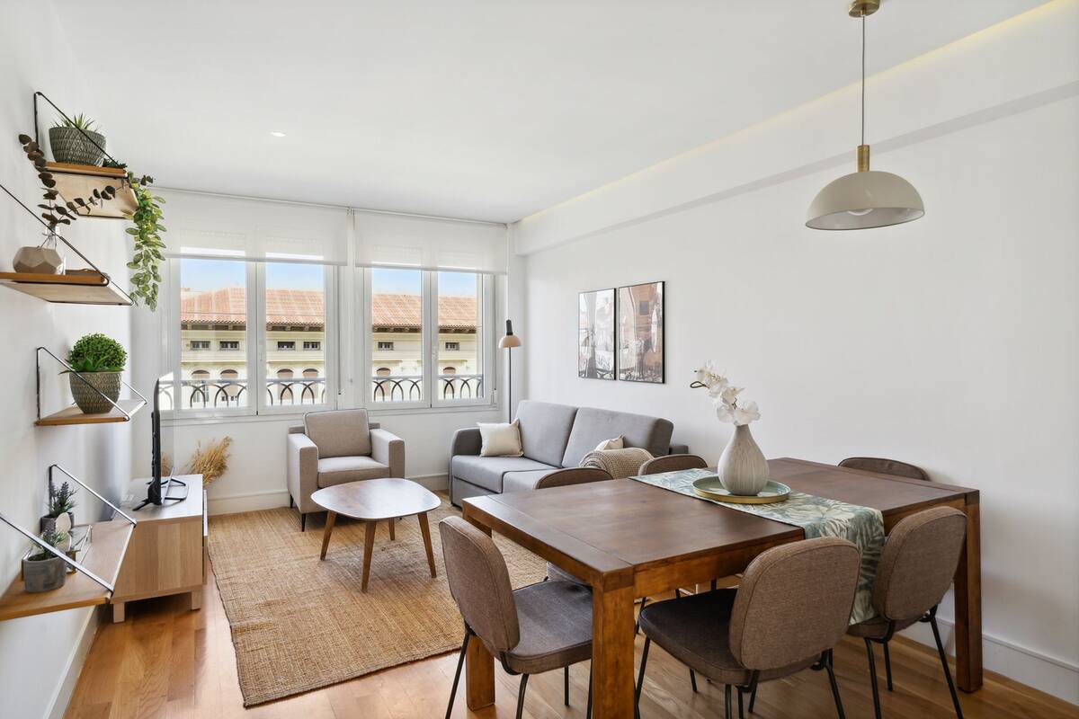 A modern living room with a dining area, large windows, and a view of buildings.
