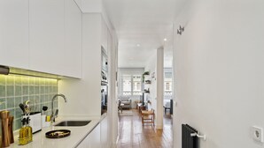 A modern kitchen with white cabinets, a black countertop, and a wooden floor leading to a dining area with a white chair and table. - Limehome Madrid Calle de Nuñez de Balboa (Madrid)