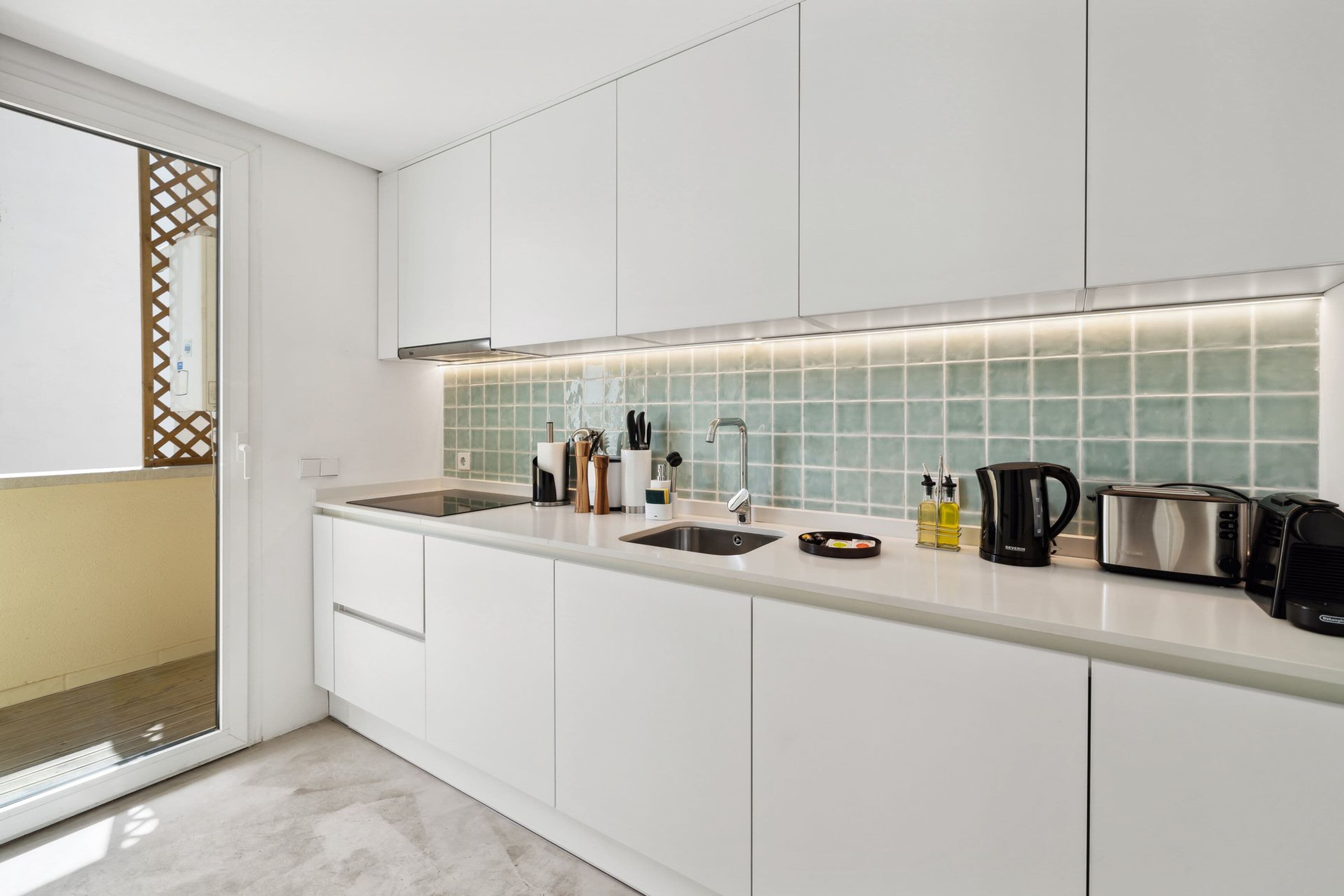 A modern kitchen with white cabinets, a stainless steel sink, and a tiled backsplash.