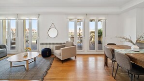 A spacious living room with a wooden dining table, comfortable seating, and large windows offering a view of the outdoors. - Limehome Madrid Calle de Nuñez de Balboa (Madrid)