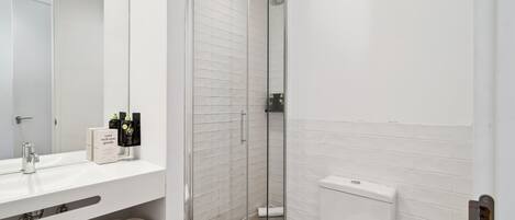 A modern bathroom with a glass-enclosed shower, a white sink, and a toilet.