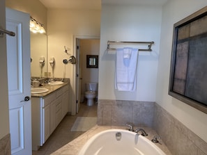 A modern bathroom with a double sink vanity, a large bathtub, and a toilet.