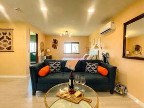 A living room with a sofa, a glass coffee table with a bottle and glasses, a magazine rack, and a window with natural light. - Luxury Bungalow w/Private SAUNA.A beautiful spot to unwind, surrounded by nature (Horseheads)