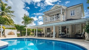 A poolside area with a large pool, outdoor seating, and a two-story building with a balcony.