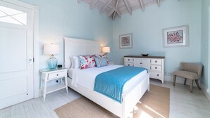 A bedroom with a bed, bedside tables, a dresser, a chair, and artwork on the walls.