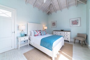 A bedroom with a bed, bedside tables, a dresser, a chair, and artwork on the walls.