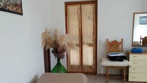 Un dormitorio con cama, una silla, cómoda, espejo y una puerta con cortinas.