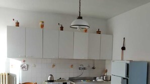 Una cocina compacta con armarios blancos, lavadora, una mesa con mantel colorido y una lámpara colgante.