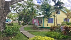 A yellow house with a porch, surrounded by lush greenery and a pathway. - Bliss 2 Bedroom Home by Bluescape (Holetown)