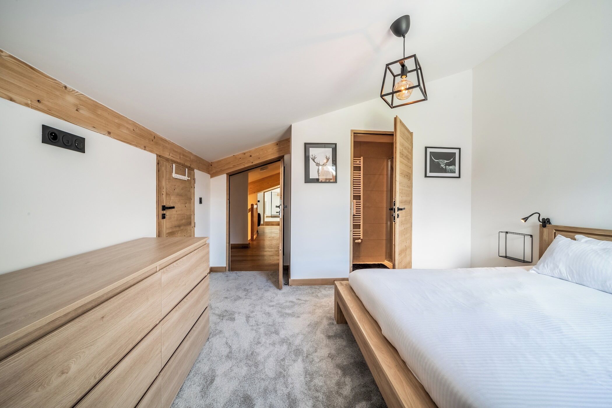 Ein modernes Schlafzimmer mit einer hölzernen Bank, einem Bett und einem Gang zu einem weiteren Raum.