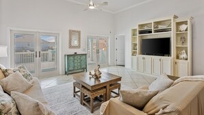 A spacious living room with a large TV, a ceiling fan, and a view of the outside. - Pair-a-dice 3 Bedroom Home by RedAwning (Port Bolivar)