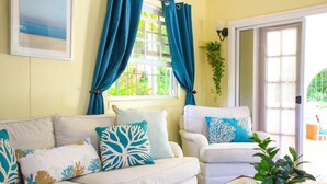 A living room with a sofa and armchairs, a glass coffee table, and a view through a window with blue curtains. - Aqua Bliss 3 Bedroom Home by Bluescape (Holetown)