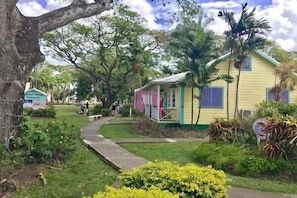 Welcome to a charming single-story home surrounded by lush greenery and palm trees, with a cozy porch and a simple, functional design.