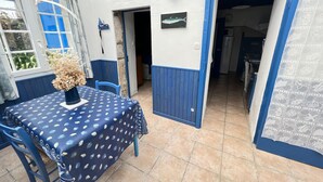 Un coin repas avec une table dressée pour deux personnes, une nappe à motifs bleus et blancs, et un vase contenant des fleurs séchées.