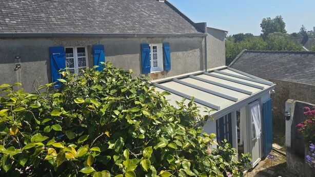 Une maison avec un toit en pente, des volets bleus et une véranda.