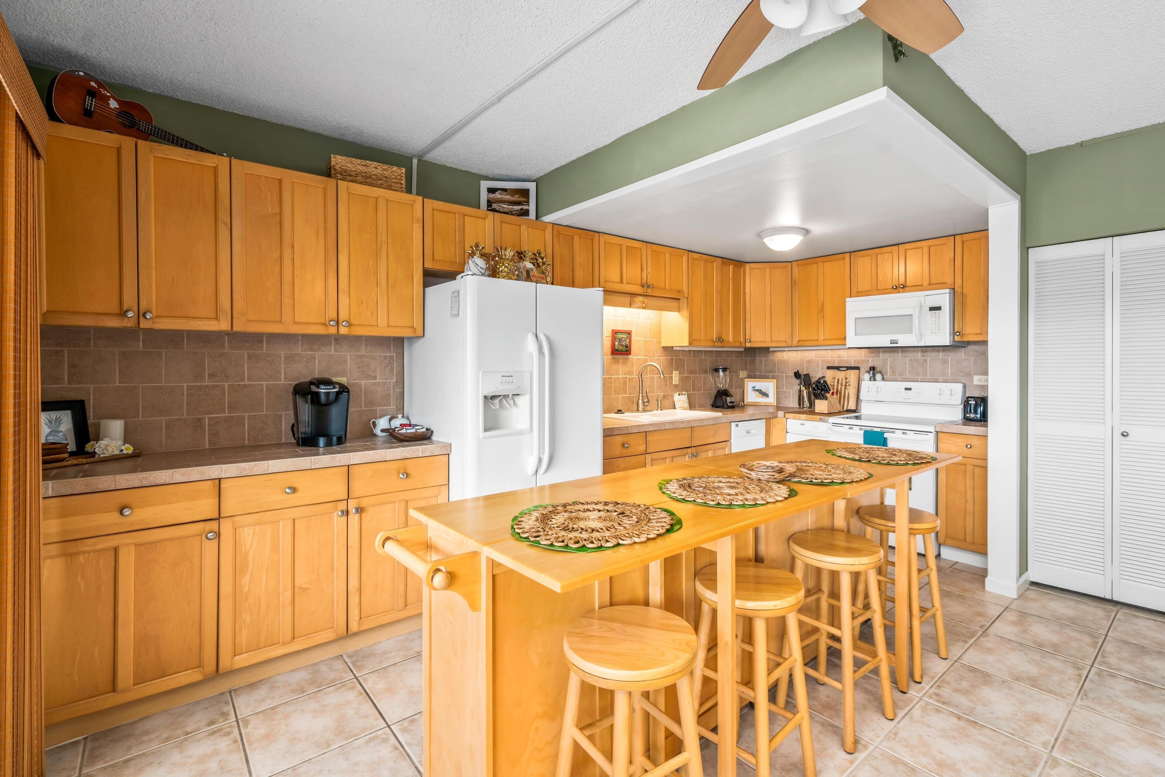 A kitchen with wooden cabinets, a white refrigerator, a microwave, and a bar area with stools.