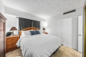 Un dormitorio con una cama grande, cabecera de madera, dos mesitas de noche con lámparas, un aparador y una puerta.