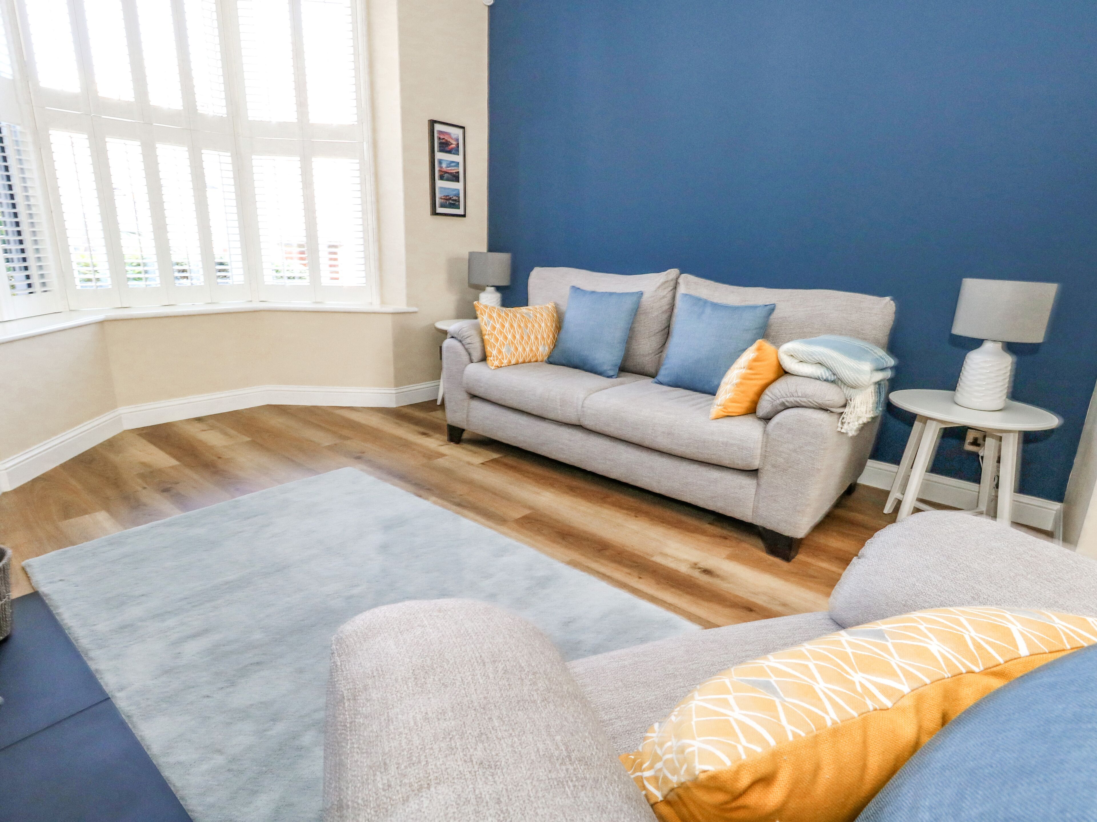 A living room with a grey sofa, a blue accent wall, and a wooden floor.