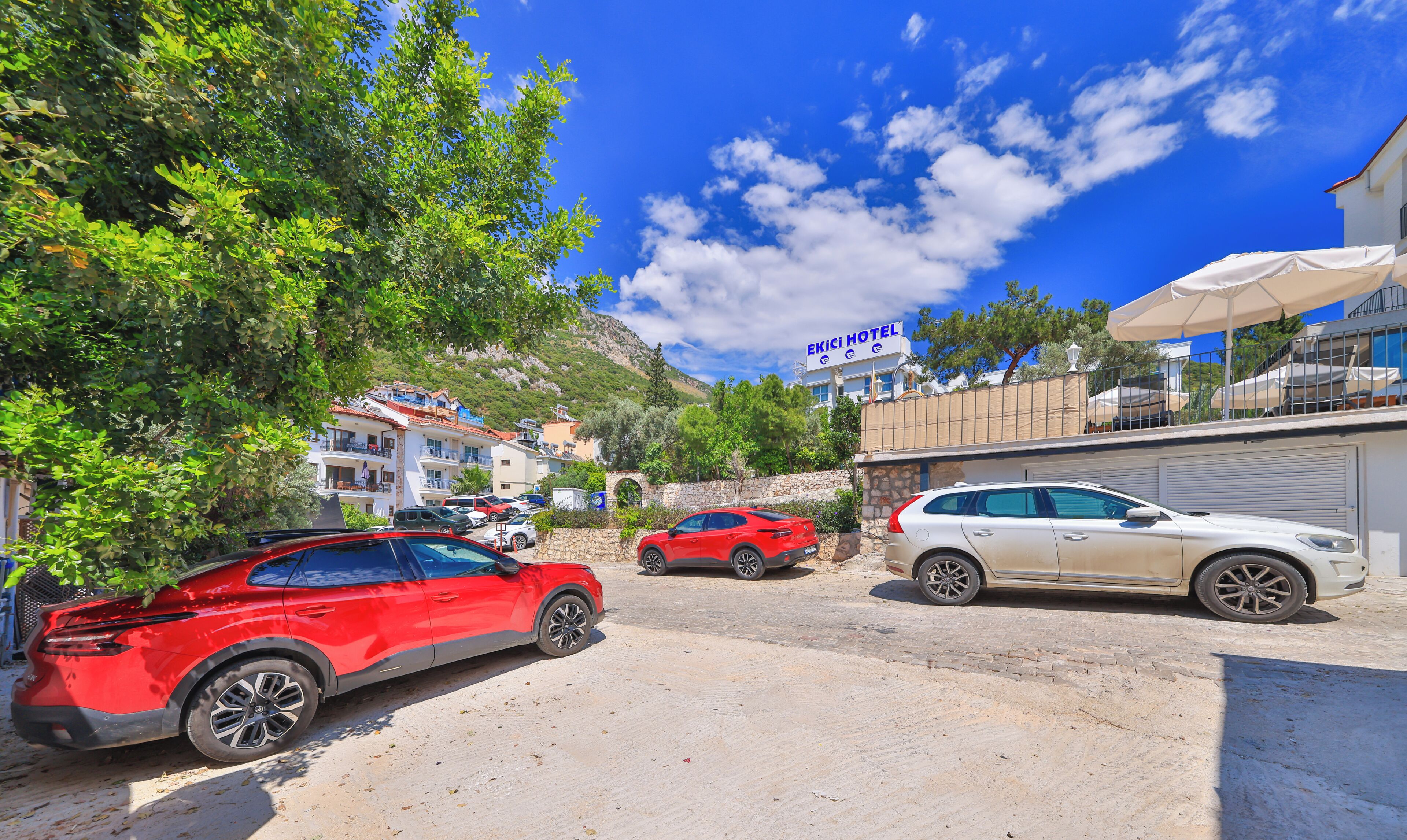 Un hotel con pared de piedra, coches estacionados y cielo azul despejado.