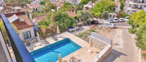 A residential area with a swimming pool, lounge chairs, and a paved walkway.