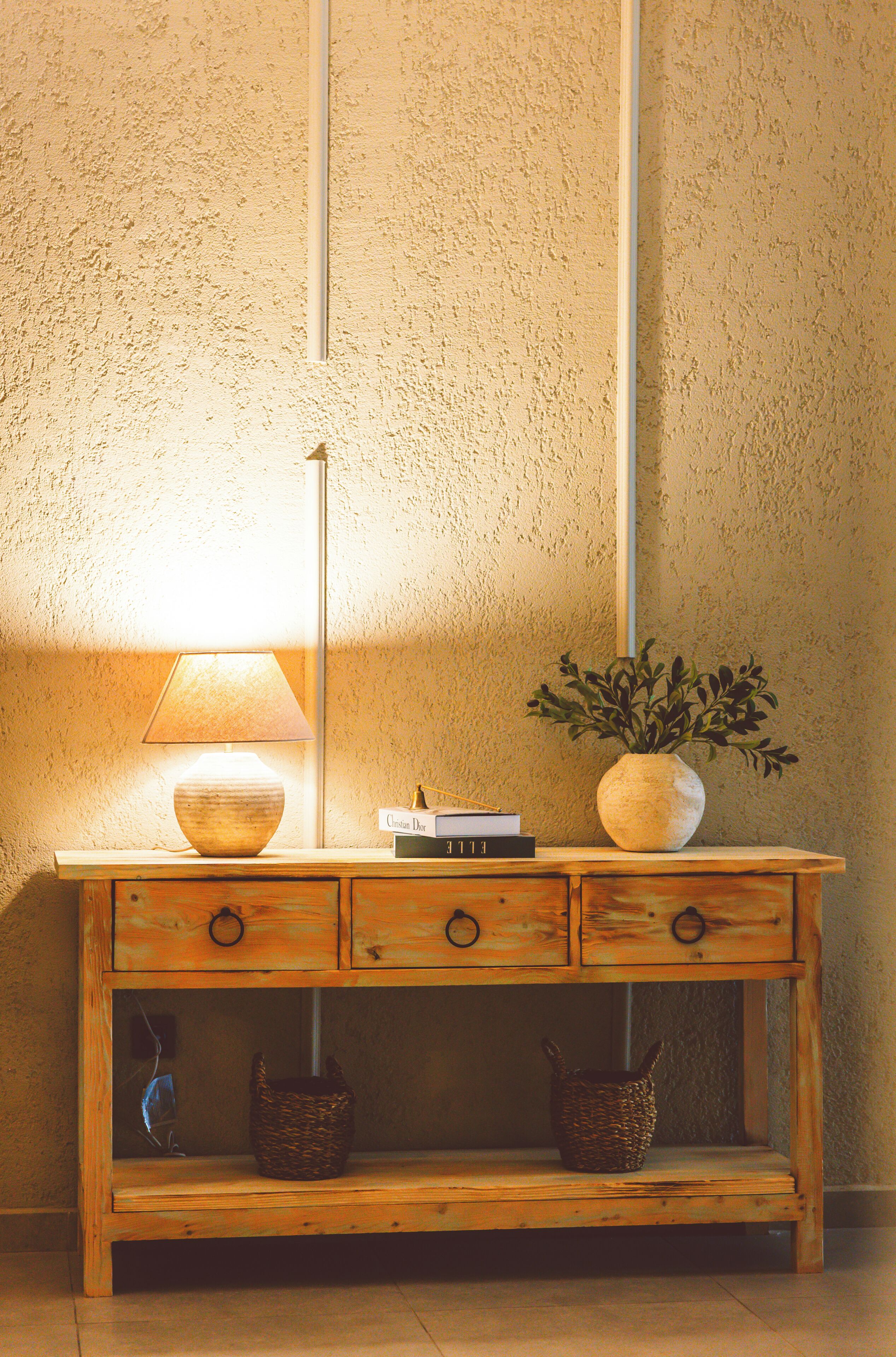Une console en bois, sur laquelle sont posés une lampe, un vase avec des plantes et deux paniers.