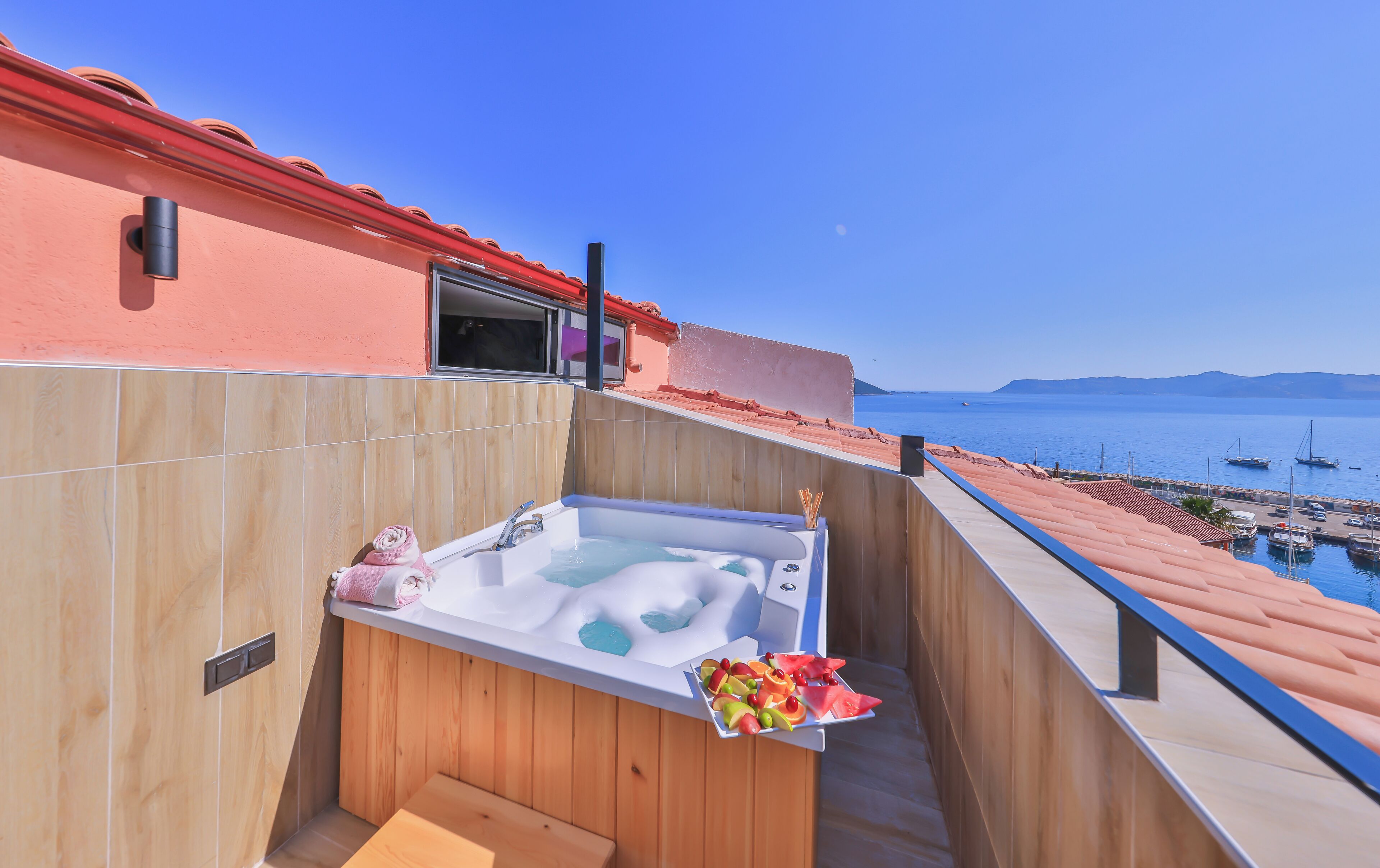 A balcony with a hot tub, wooden flooring, and a view of the sea and boats.