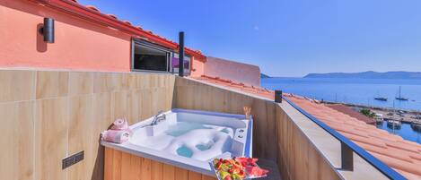 A balcony with a hot tub, wooden flooring, and a view of the sea and boats.