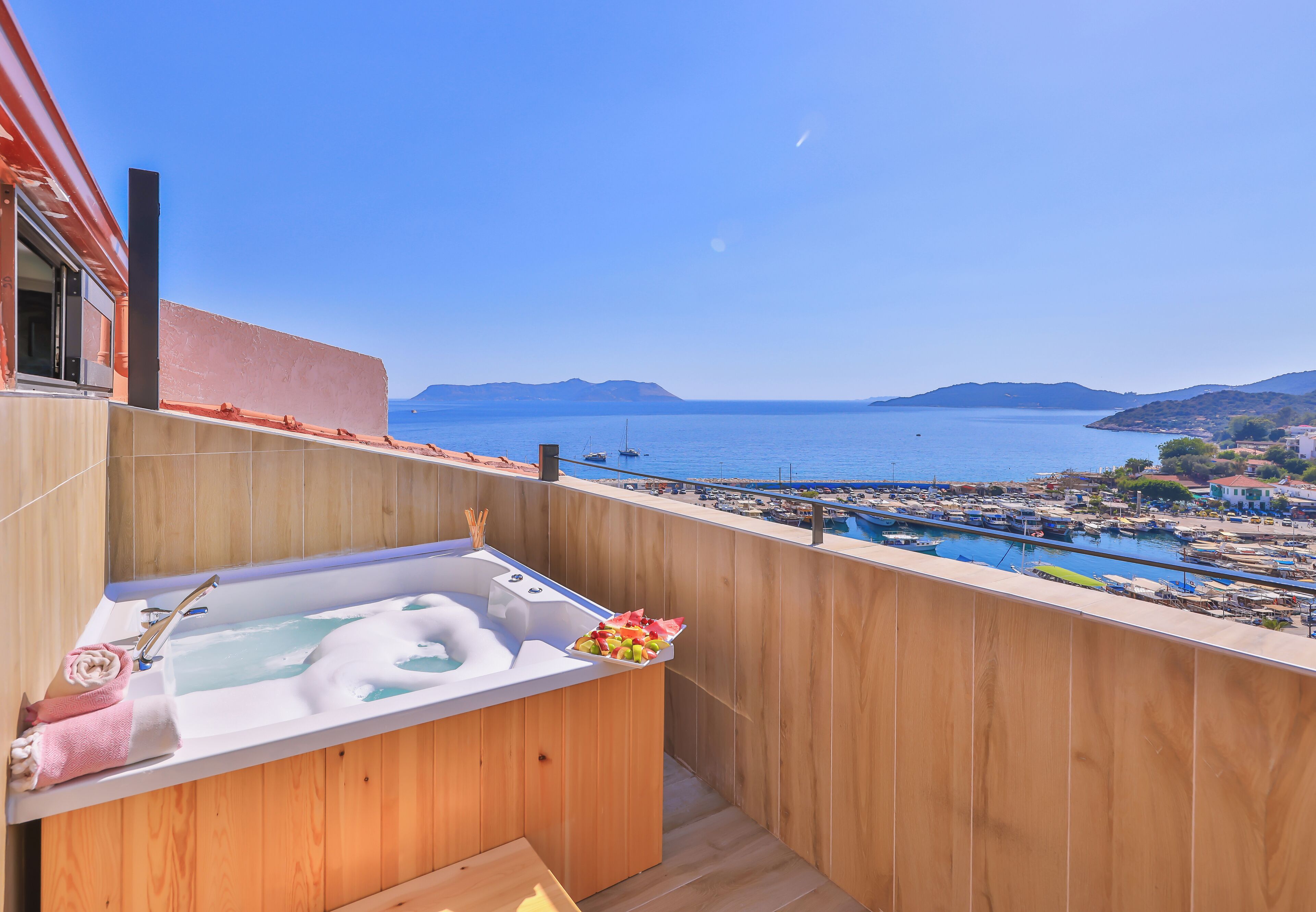 Un balcón de madera con un jacuzzi, vista al mar y un puerto deportivo.