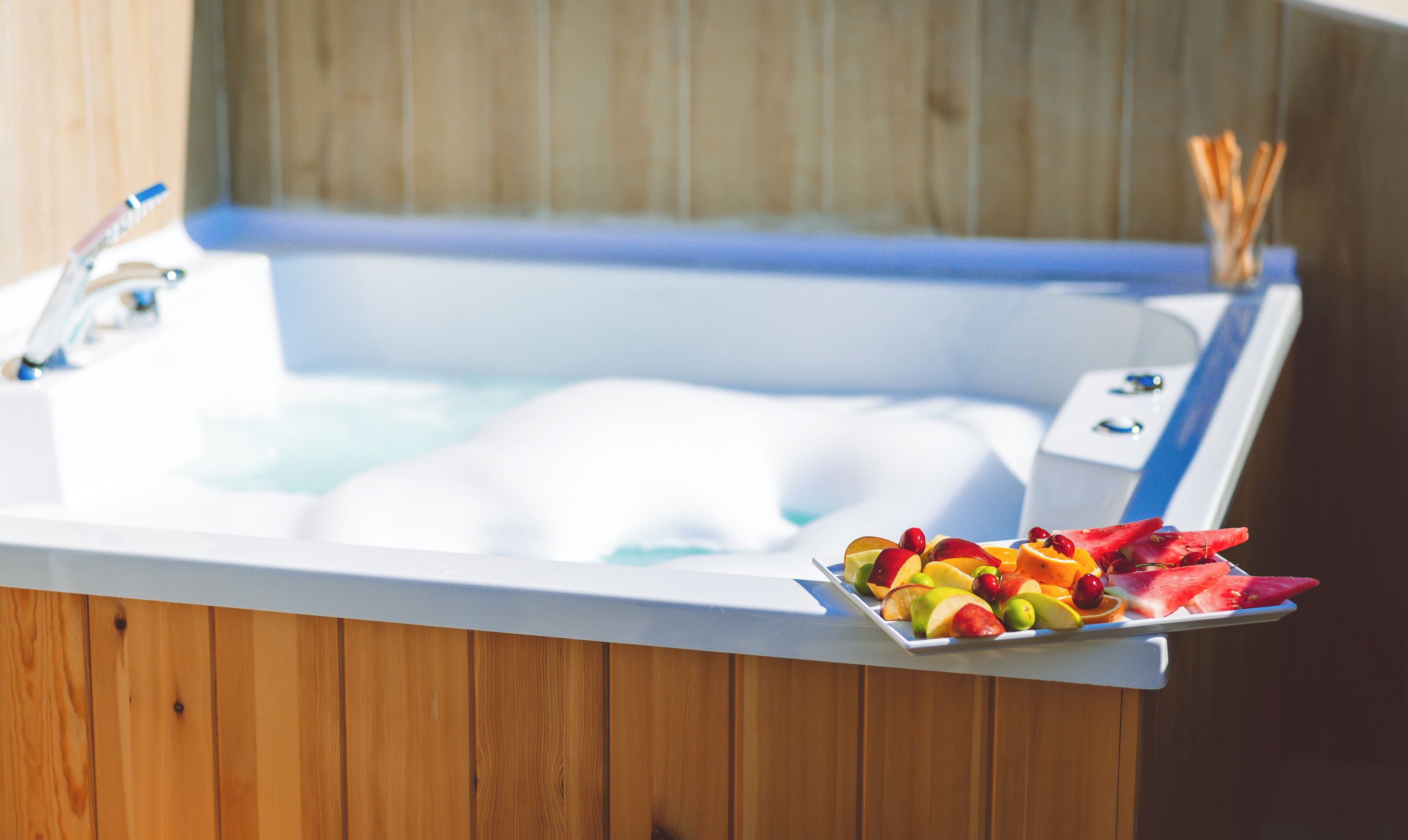 A bathtub with a tray of fruits and a bottle of water.