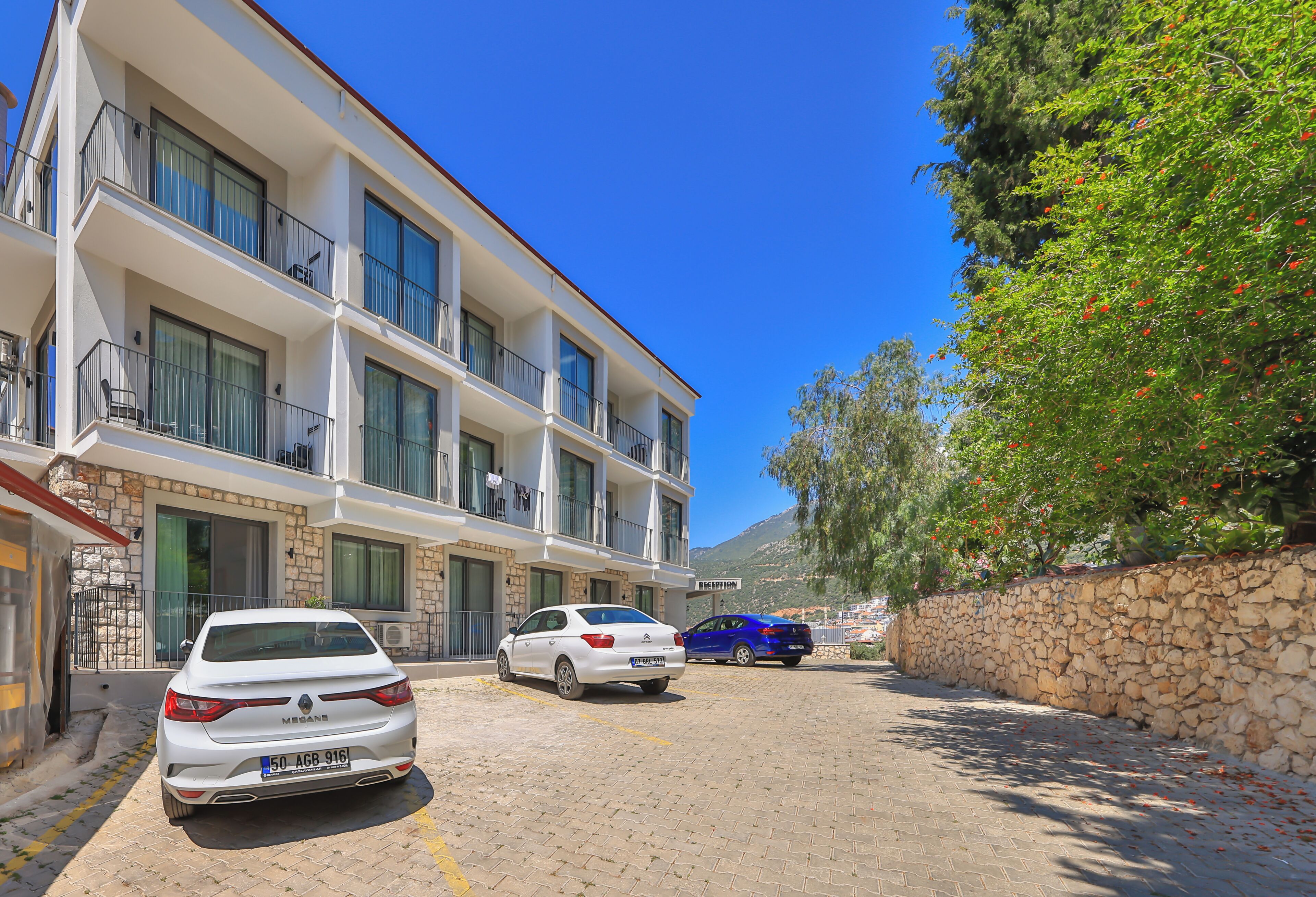 A multi-story building with balconies, a stone wall, and a parked car.