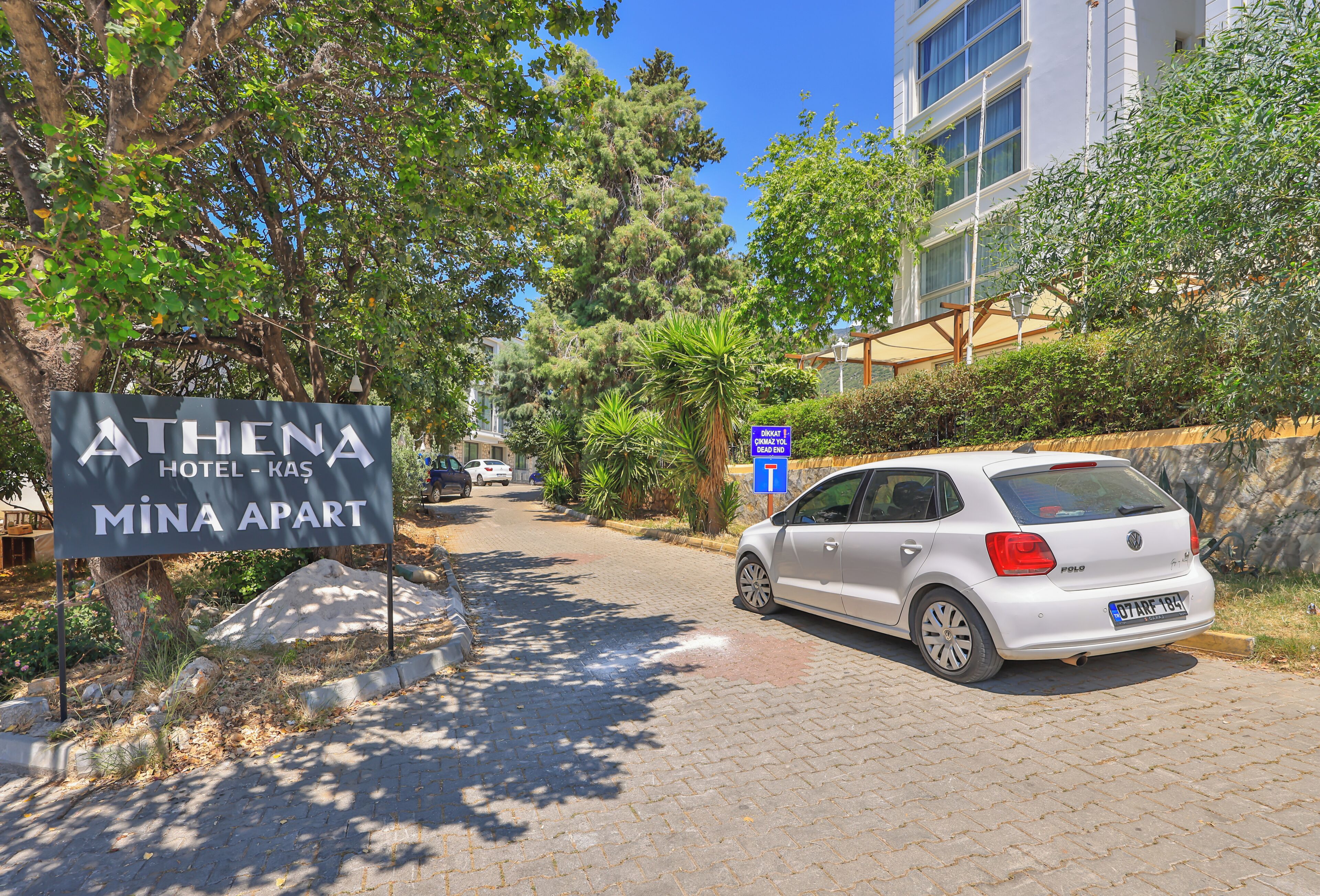 A paved driveway leading to a building with a sign for 'ATHENA HOTEL - KAS MİNA APART.'
