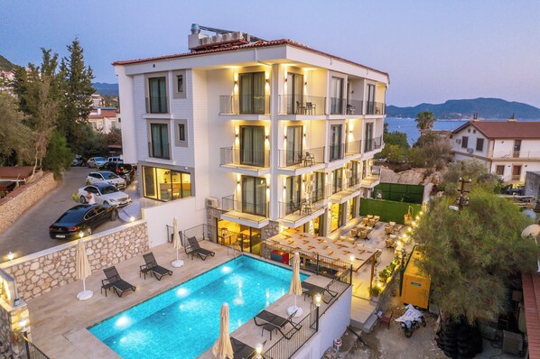 Un hotel de varios pisos con piscina, mobiliario exterior y balcones.