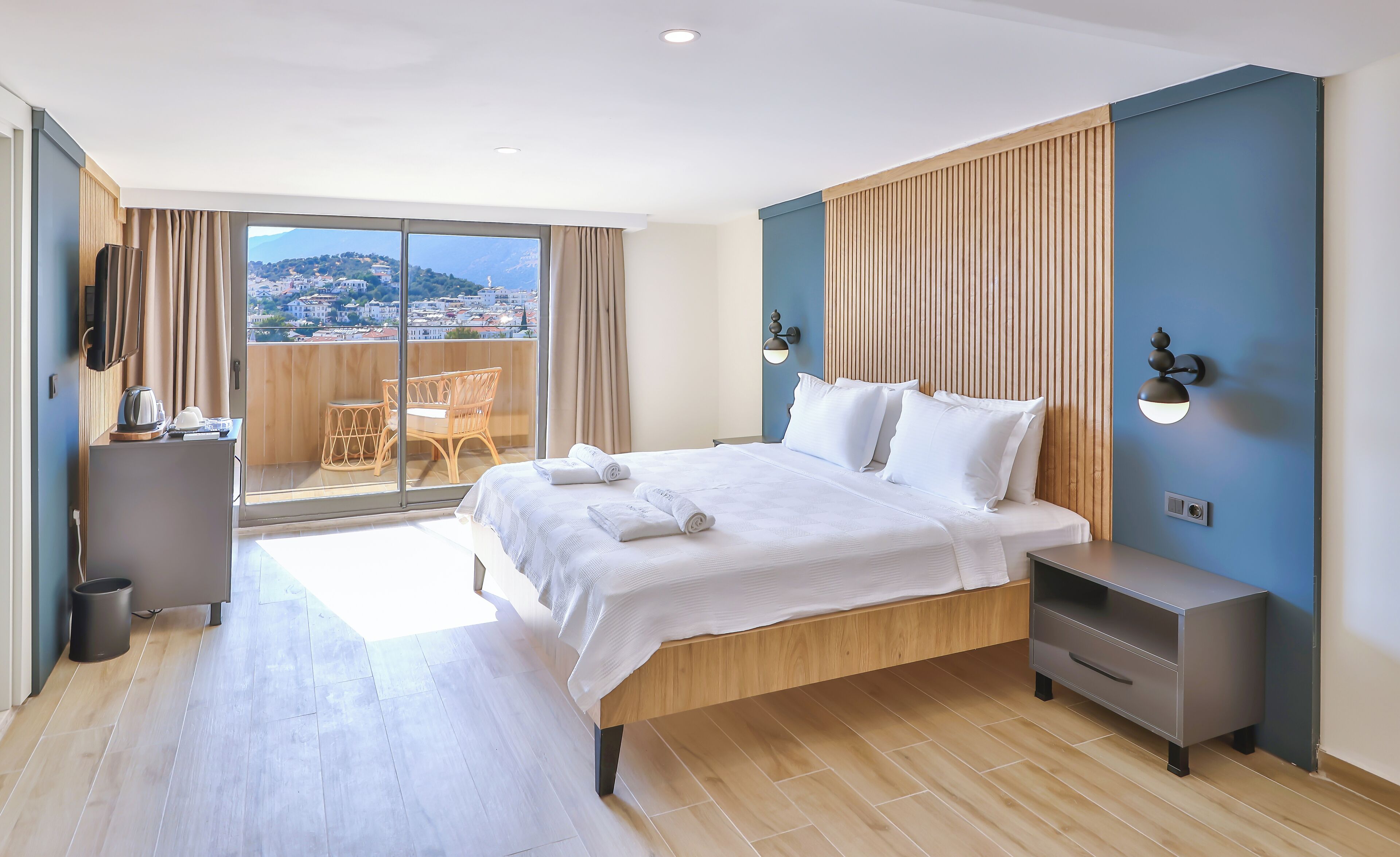 Een moderne hotelkamer met een groot bed, een nachtkastje, een televisie en een balkon met uitzicht over de stad.