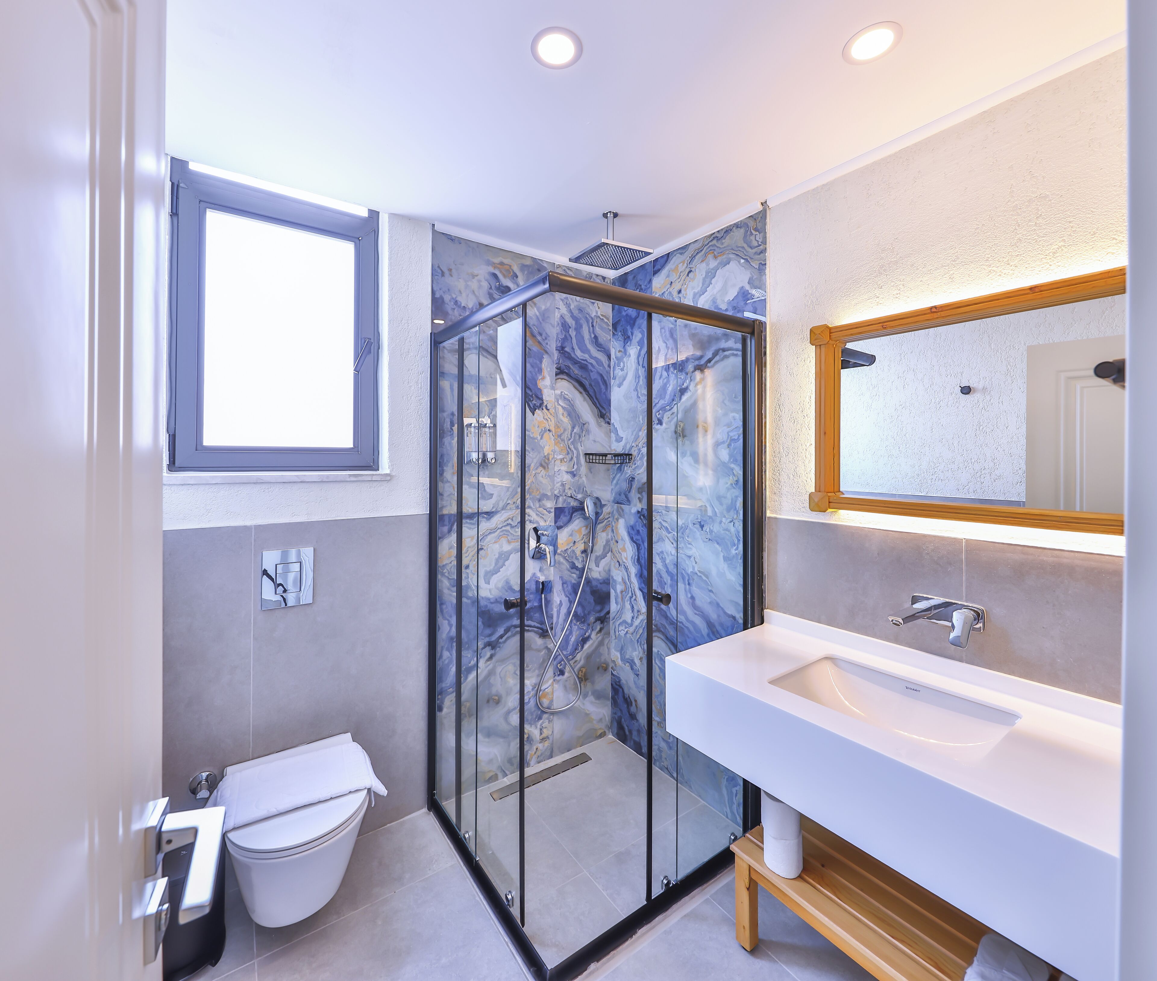 A modern bathroom with a glass shower enclosure, a white sink, and a marble backsplash.