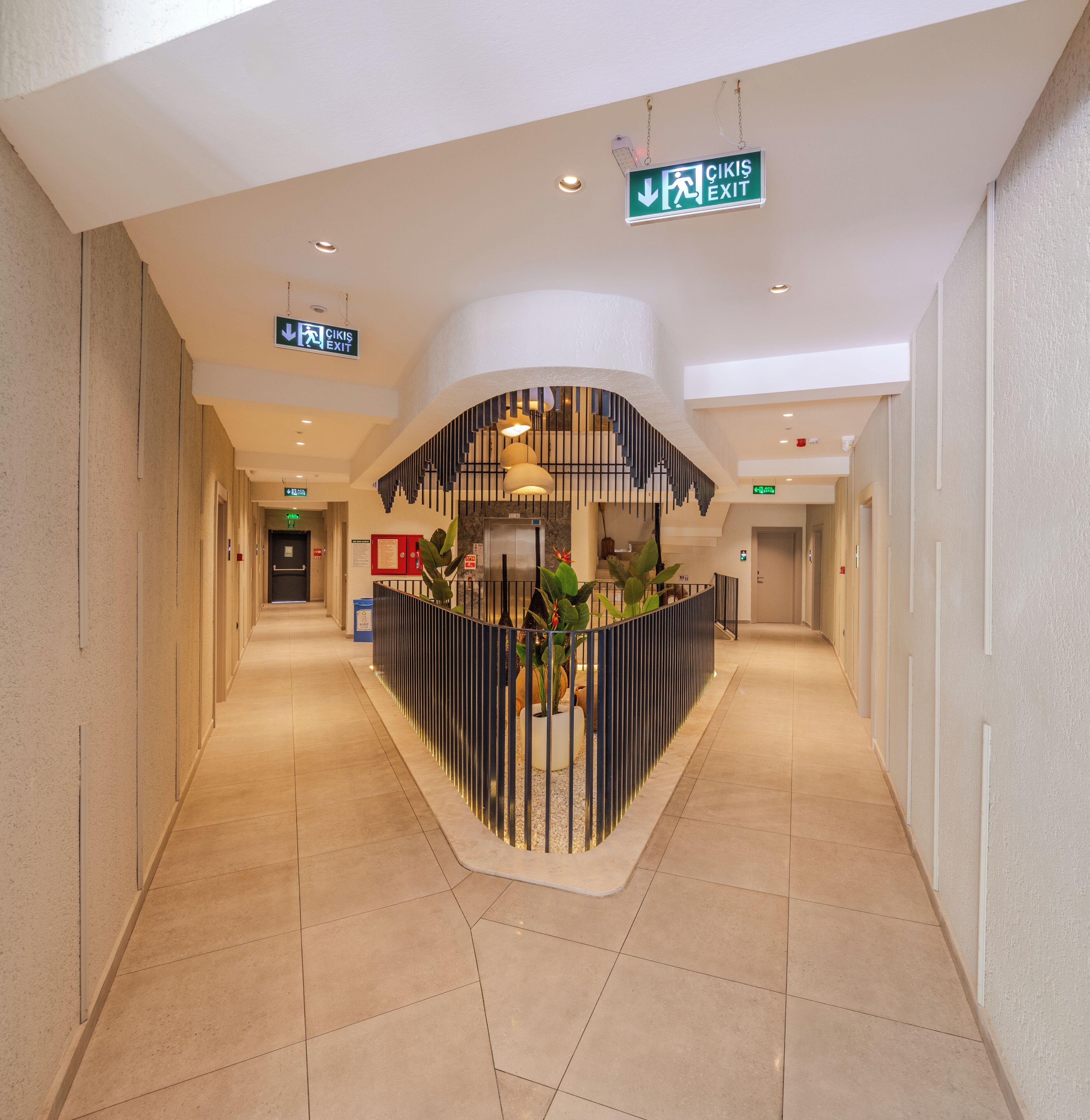 A hotel lobby with a central reception desk, multiple exit signs, and a tiled floor.