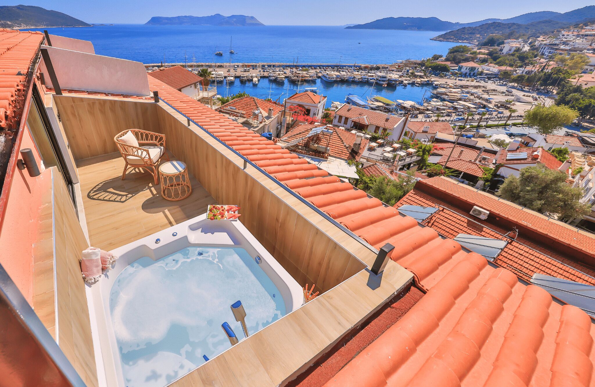 A rooftop terrace with a hot tub, seating area, and a view of a marina and coastal town.